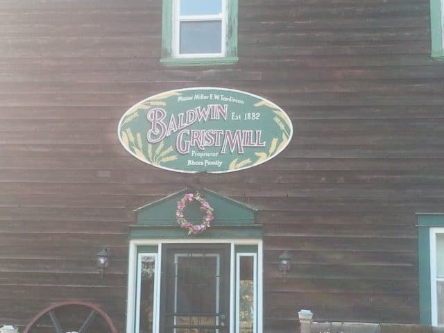 brown cabin with green borders around the white windows, oval green and yellow sign, glass door below the sign