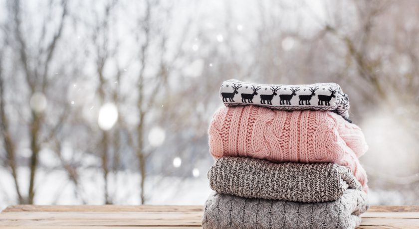 Stack of knitted sweaters on wooden tableon winter nature background.